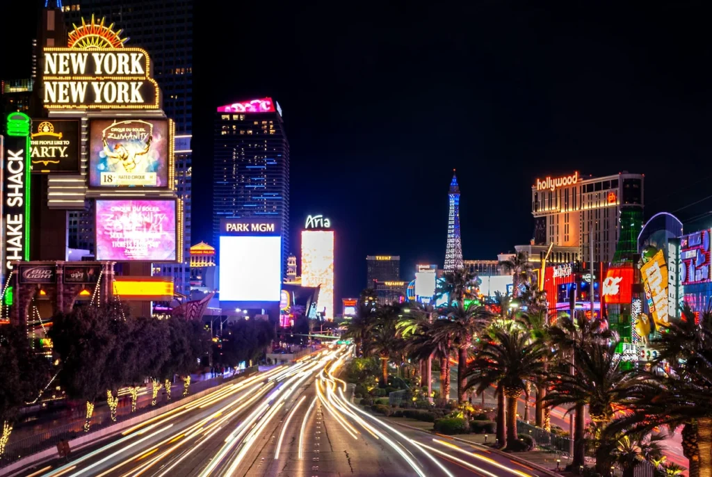 Night view of the Las Vegas Strip with long exposure car light trails between illuminated casino towers like New York-New York and Aria