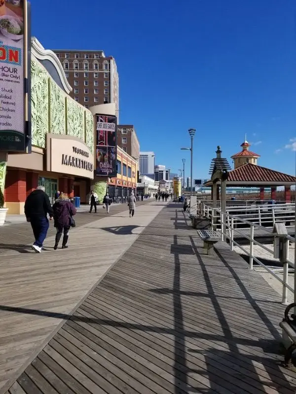 A sunny day on Atlantic City's Famous Boardwalk with people walking past shops and casinos.