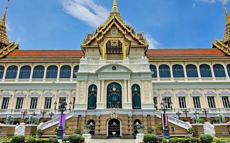 The ornate Grand Palace building shines under blue skies in Bangkok.