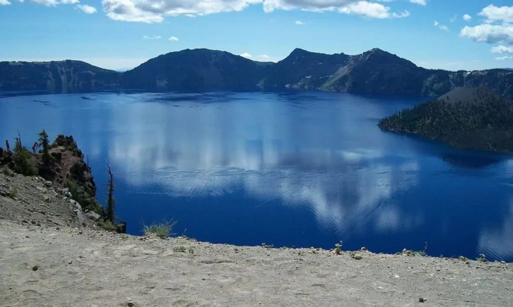 Deep blue lake surrounded by mountains under a bright sky at Crater Lake National Park.