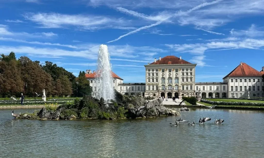 Nymphenburg Palace with a large fountain and pond in the foreground on a sunny day.