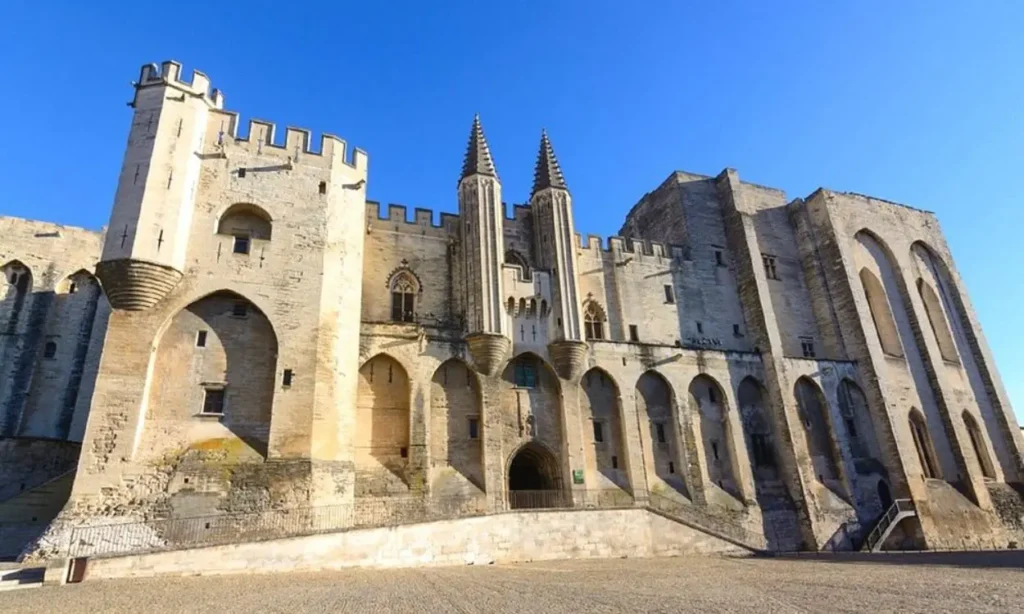 The grand stone façade of Palais des Papes stands tall under a bright blue sky.
