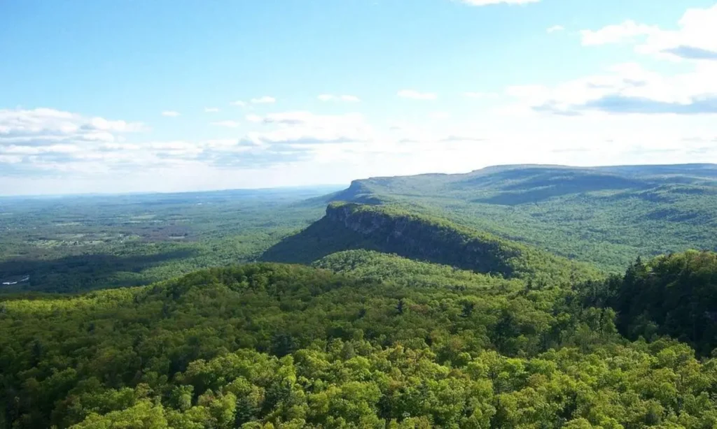 The Shawangunks ridge stretches across a vast green forested landscape under a bright sky.