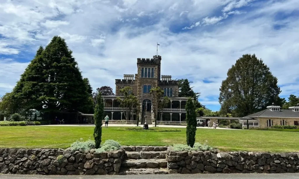 Historic stone building with a tower surrounded by gardens and trees in Dunedin.