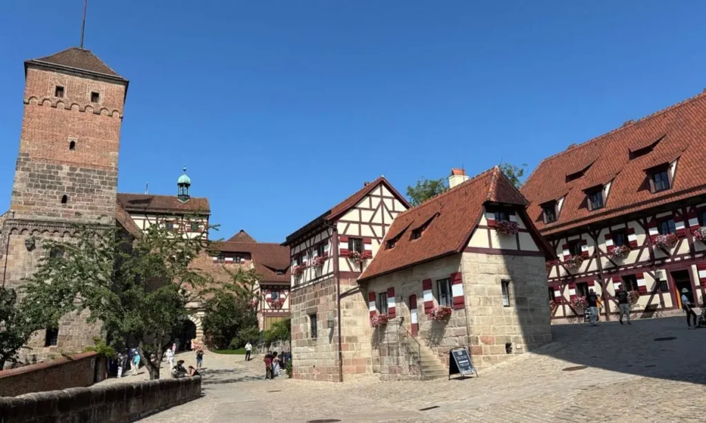 Historic buildings with red roofs inside Nuremberg Castle courtyard on a clear day.