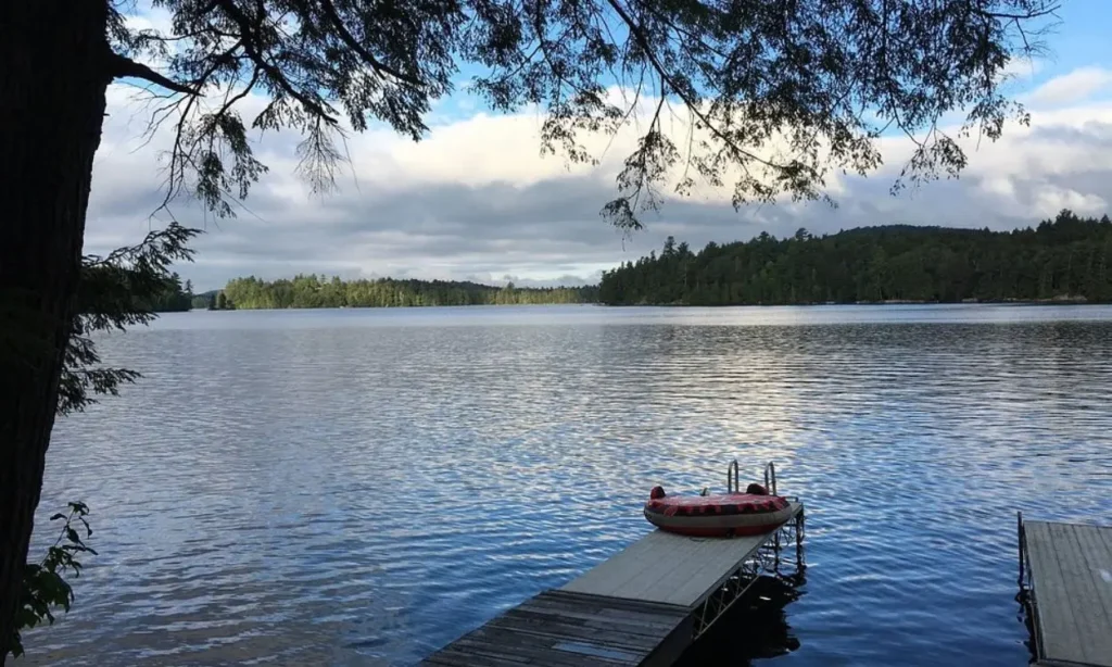 A calm view of Saranac Lake with docks and trees reflecting in the water.