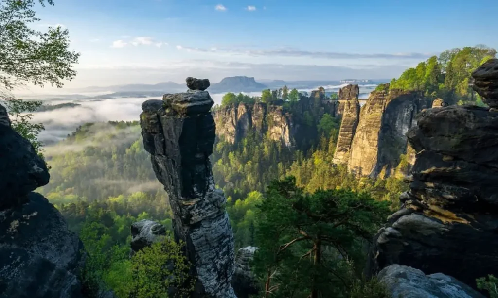 Rock formations and forest landscape in Saxon Switzerland National Park under a clear sky.