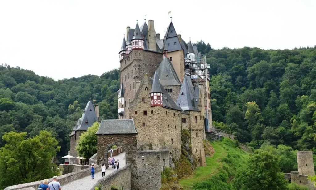 People walking toward Burg Eltz, a medieval castle surrounded by forest.