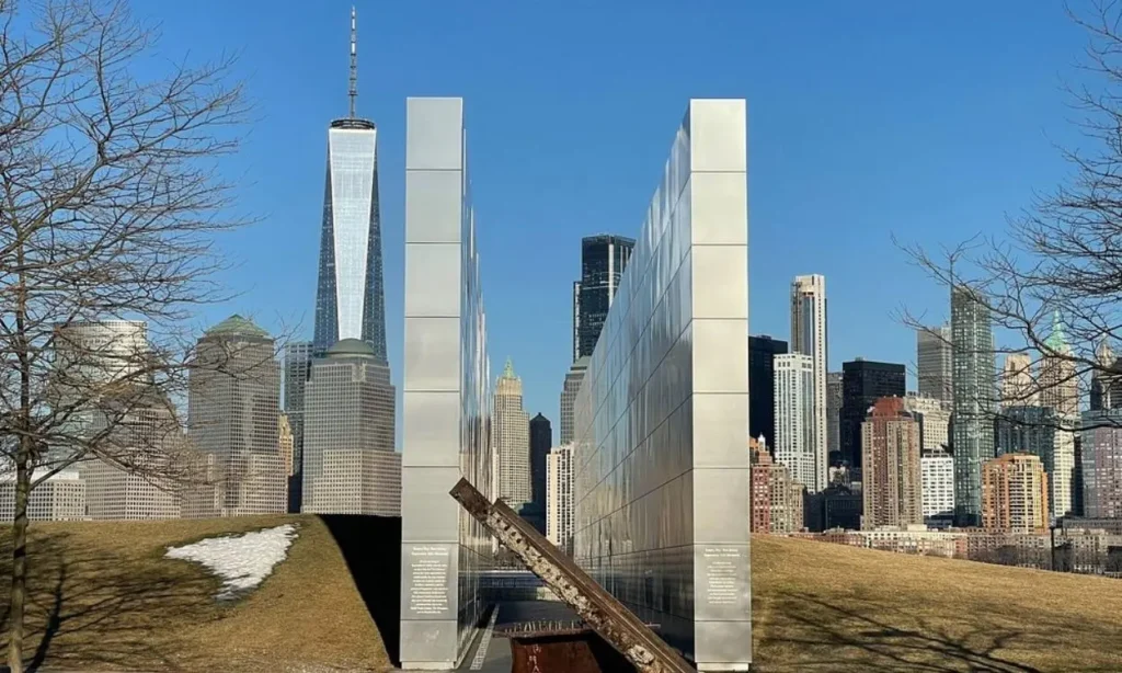 A clear view of the New York City skyline from Liberty State Park with the Empty Sky memorial in the foreground.