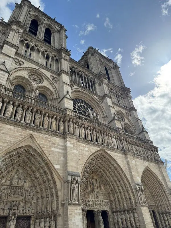 Exterior façade of the Notre-Dame Cathedral in Paris with detailed Gothic architecture and statues.