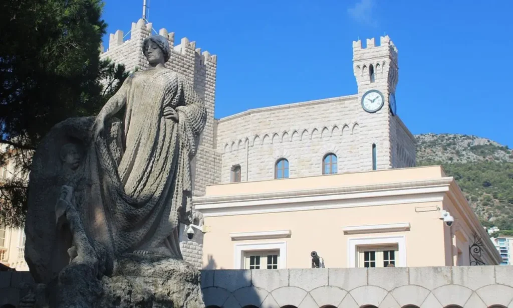A statue stands in front of The Prince’s Palace with its clock tower and stone walls.