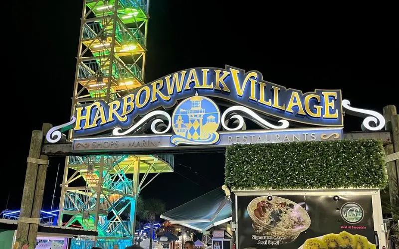 Night view of the HarborWalk Village entrance sign lit with colorful lights.