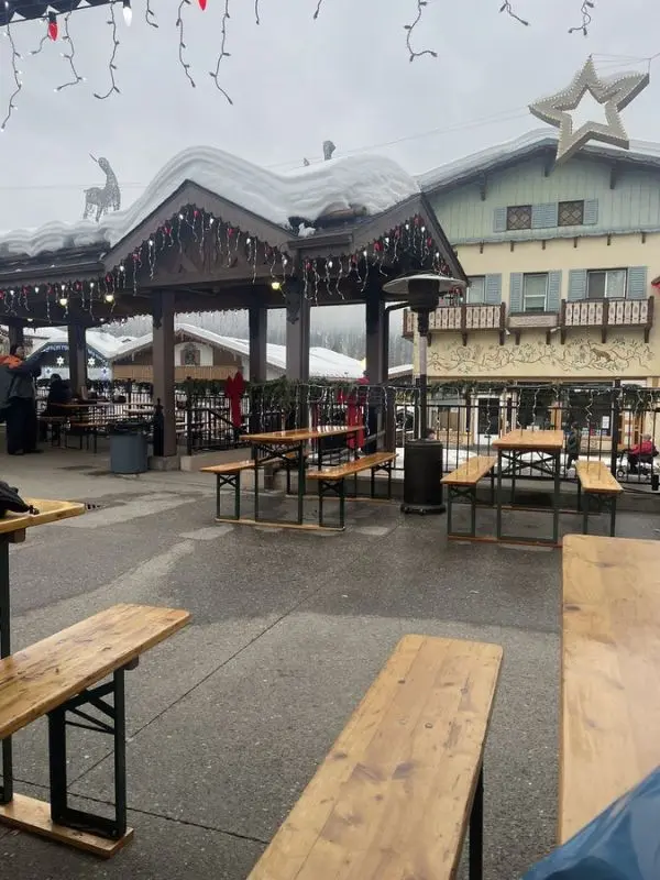 Outdoor seating area with wooden benches and snow-covered roofs at Leavenworth Sausage Garten.