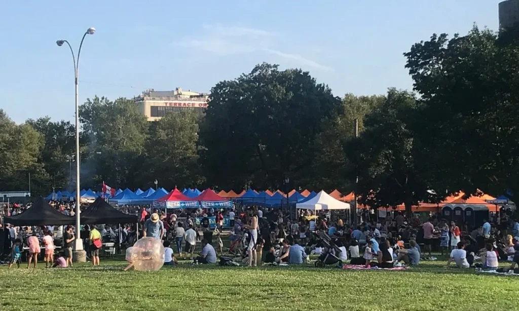 Crowds gather under colorful tents at Queens Night Market on a sunny day.
