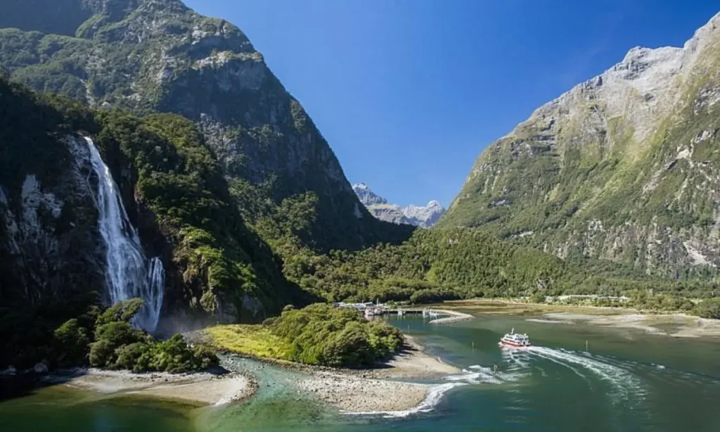 Boat cruising through a river with a waterfall and mountains in Queenstown.