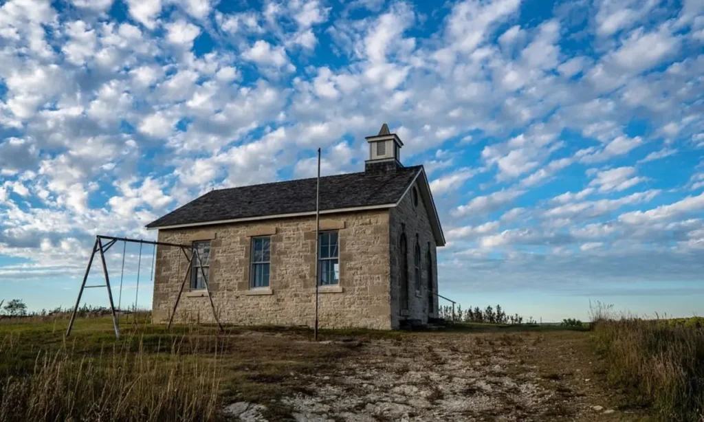 A historic stone schoolhouse at Tallgrass Prairie National Preserve beneath a blue sky.