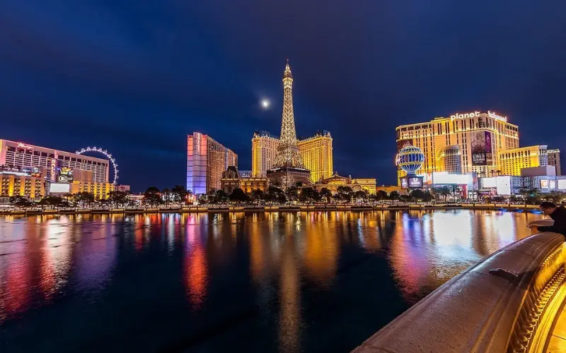 Las Vegas glows at night with brightly lit hotels and landmarks reflecting on water.