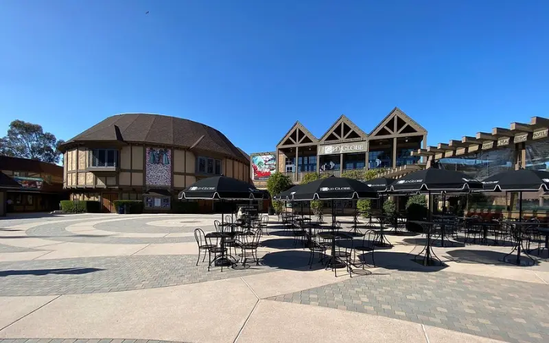 The Old Globe theater courtyard features outdoor seating under clear skies.