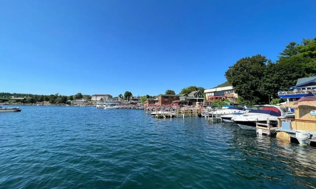 Boats line the docks along the clear blue waters of Lake George on a sunny day.