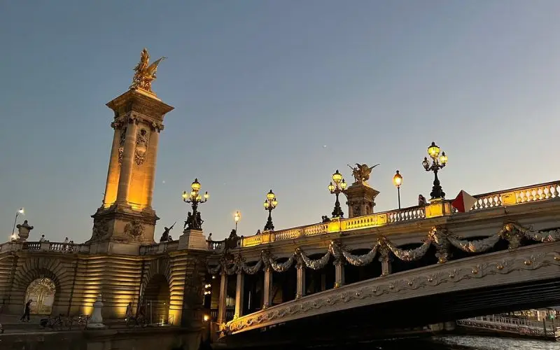 Pont Alexandre III bridge in Paris illuminated at dusk with ornate golden statues and lamps.