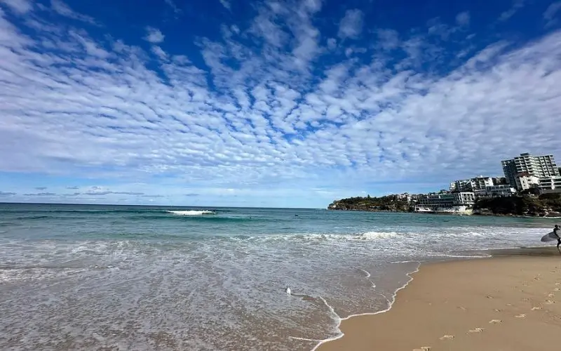 Waves washing onto the sandy shore at Bondi Beach with buildings in the distance.
