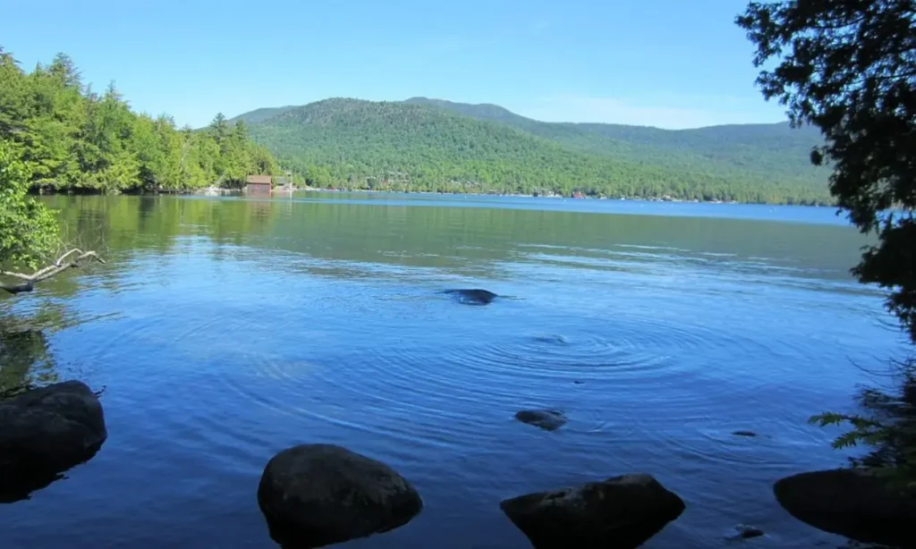 The still waters of Lake Placid reflect the surrounding green hills and trees.