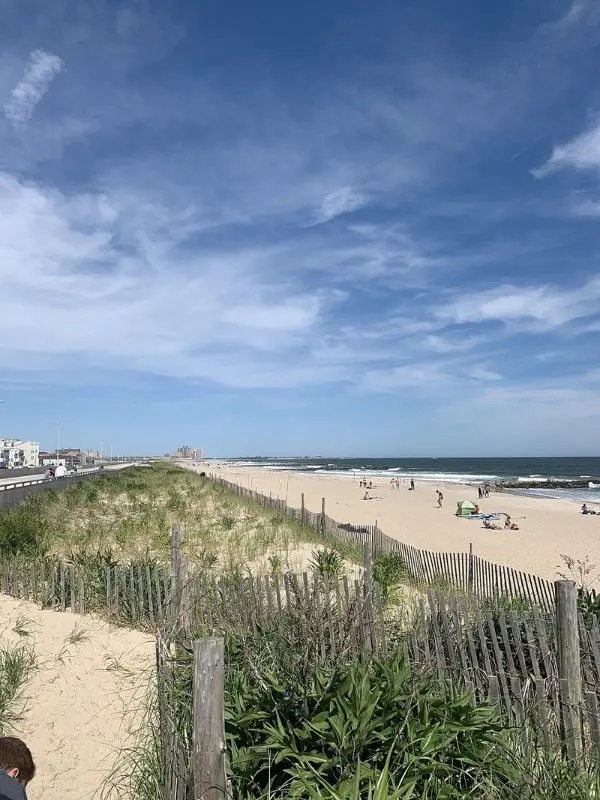 Rockaway Beach features sandy shores, grassy dunes, and a bright blue sky.