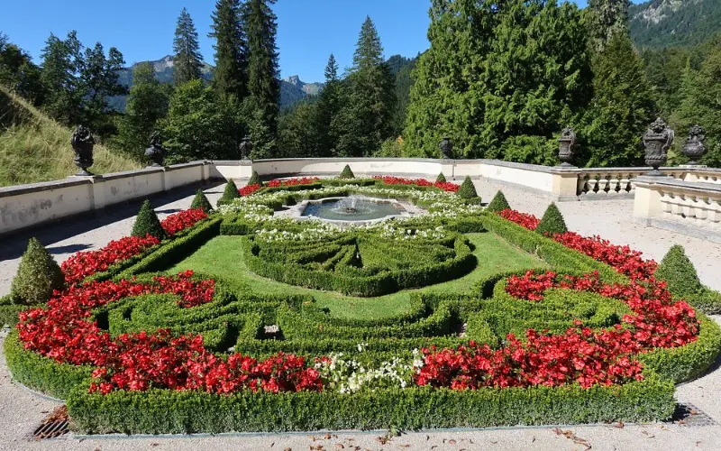 Ornate garden with red flowers and a fountain at Linderhof Palace.