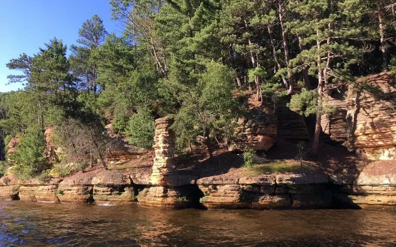 Sandstone rock formations and pine trees along the Wisconsin Dells shoreline.