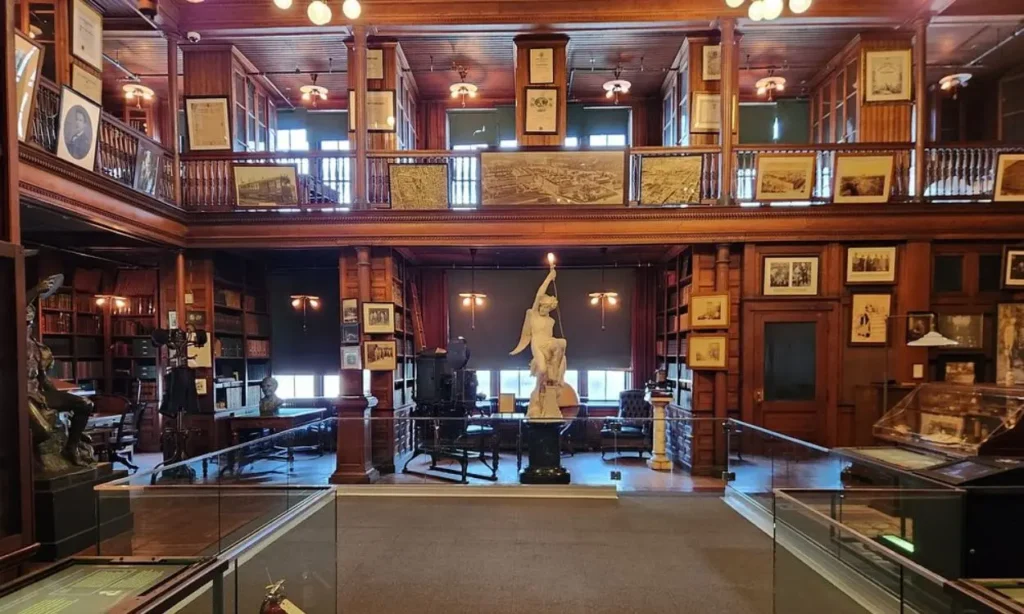 The historic library interior of Thomas Edison National Historical Park with wooden balconies, framed photos, and a central statue.
