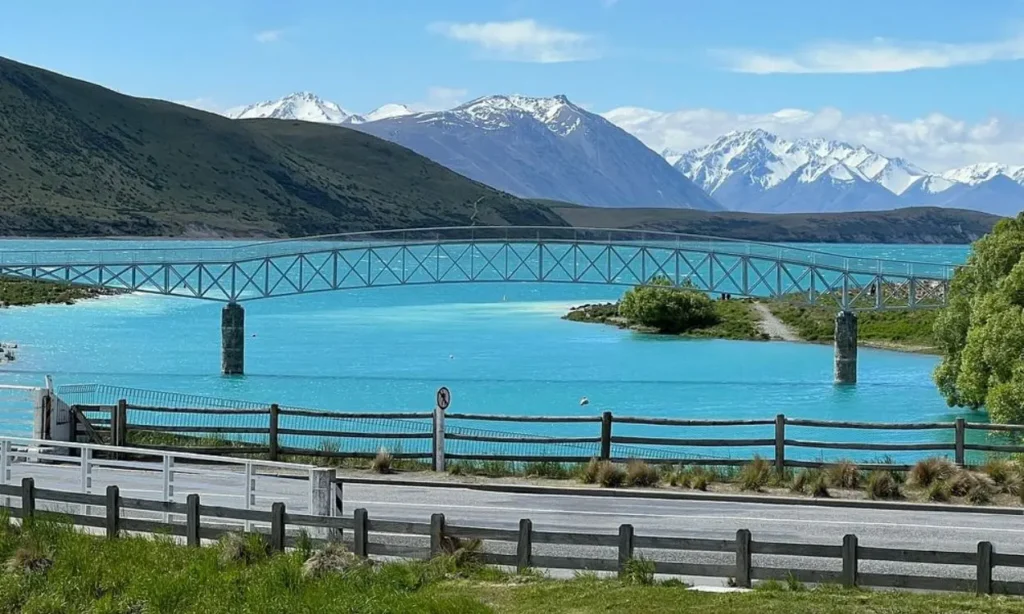 Bright blue lake with a bridge and snowy mountains in the background at Lake Tekapo.