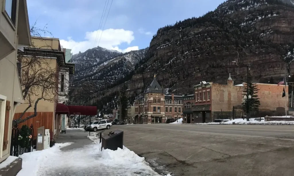 Snowy Main Street in a mountain town lined with historic buildings.