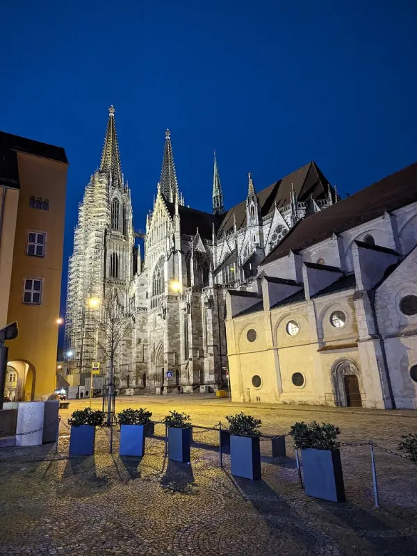 Regensburg Cathedral lit up at night with its Gothic towers.