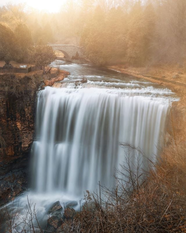 A stunning view of Hamilton Waterfalls with water cascading down the rocky cliffs, surrounded by vibrant greenery