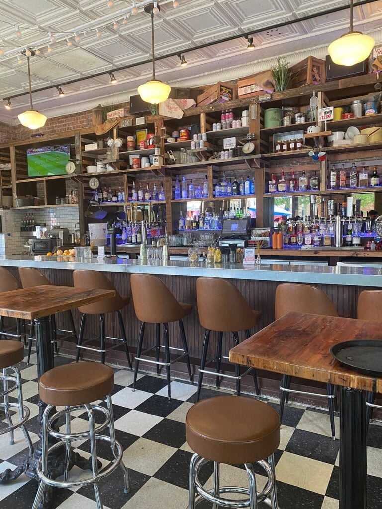 Ina Mae Tavern bar with leather stools and shelves full of bottles and decor.