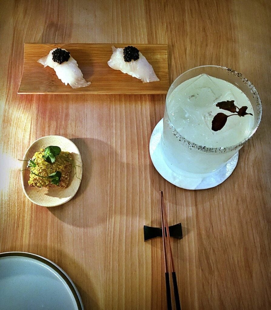 Elegant small bites and a crafted cocktail on a wooden table at Kumiko.