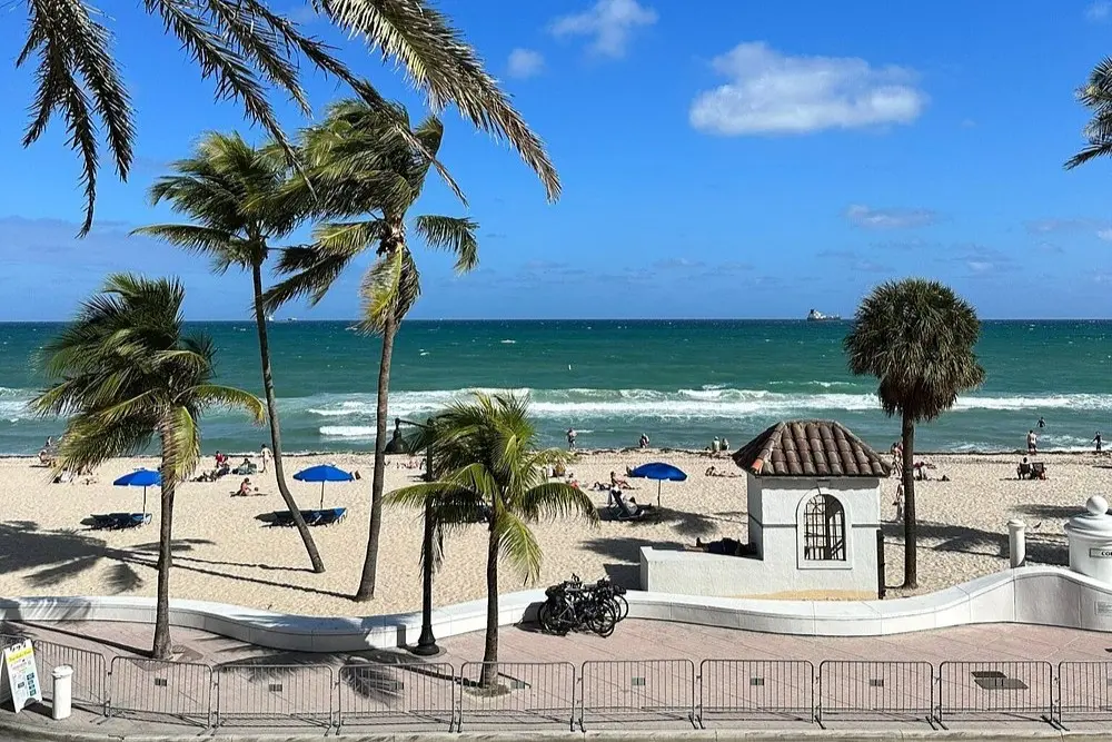 View of Fort Lauderdale Beach from Las Olas Boulevard, with palm trees, sand, and people by the ocean.