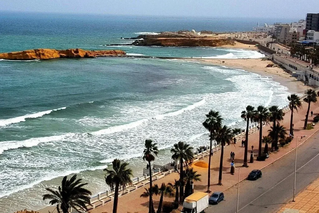 A coastal view of Sousse with palm-lined streets, sandy beaches, and turquoise waves.