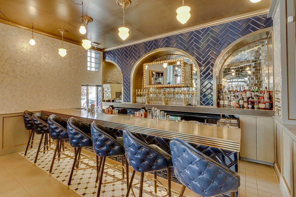 The Whale bar with blue velvet chairs, gold accents, and a mirrored back wall.