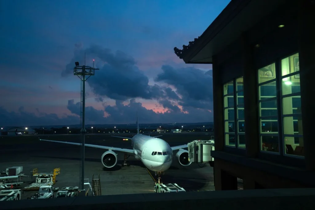 A commercial airplane parked at a terminal gate during dusk at Bali Airport