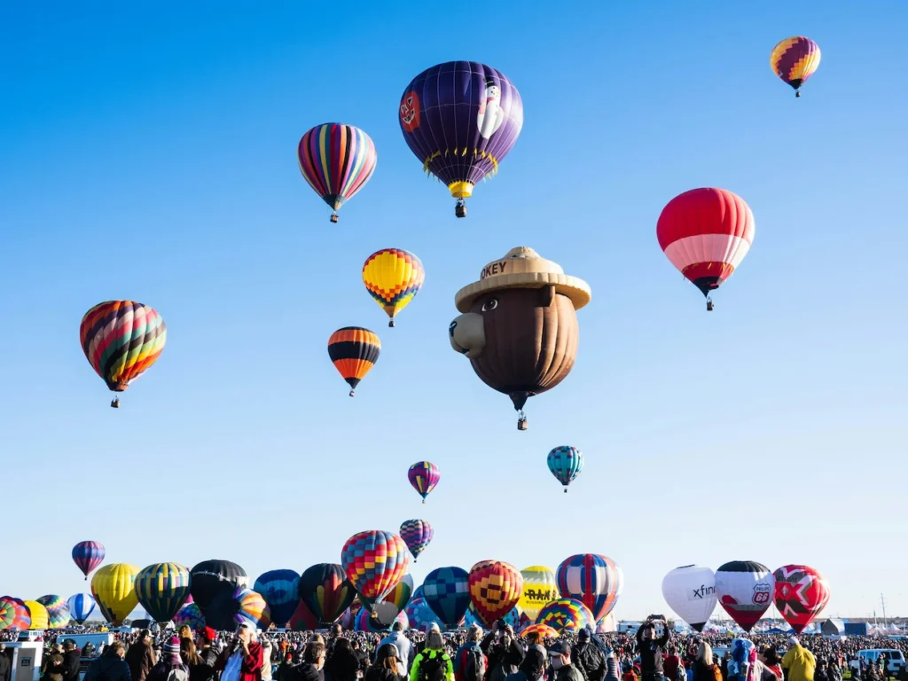 Smokey Bear hot air balloon flying among colorful balloons above a crowd