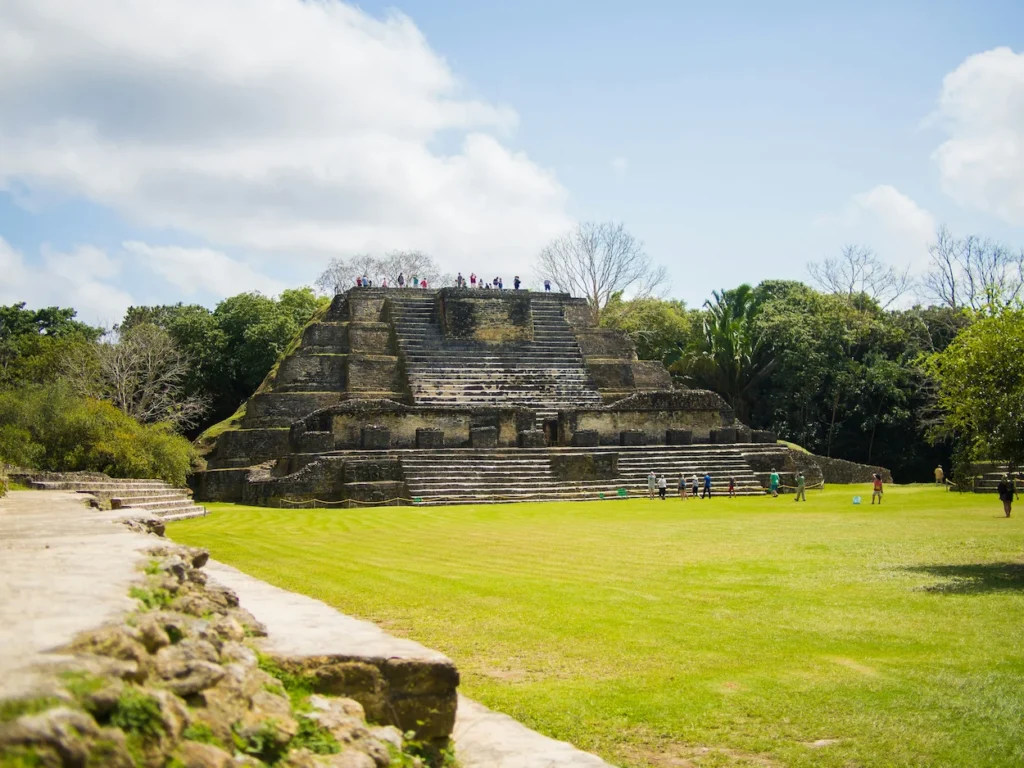 Ancient stone Mayan step pyramid surrounded by green grass fields and jungle trees in Belize