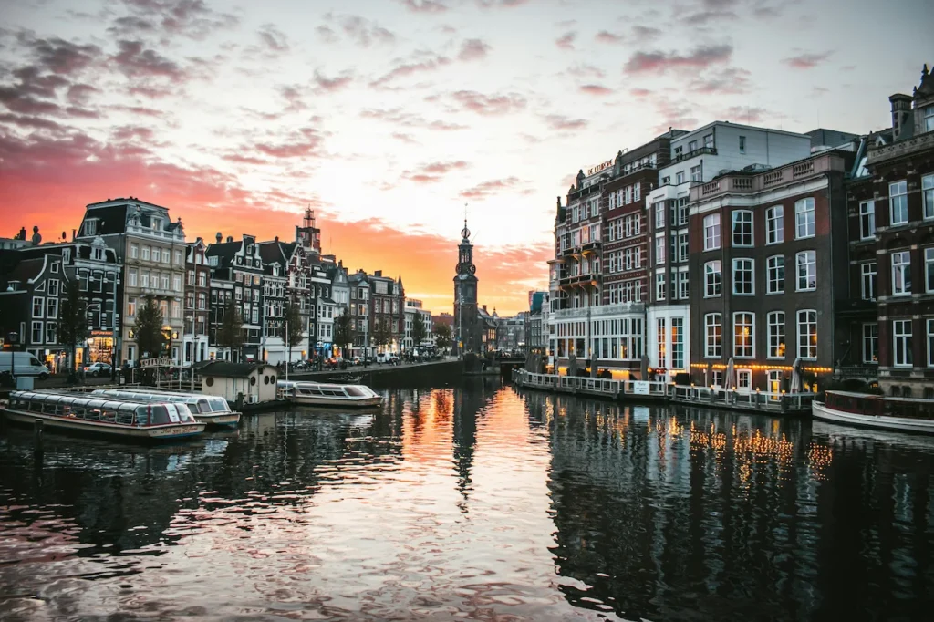 Amstel River canal at sunset with traditional buildings and the Munttoren tower in Amsterdam