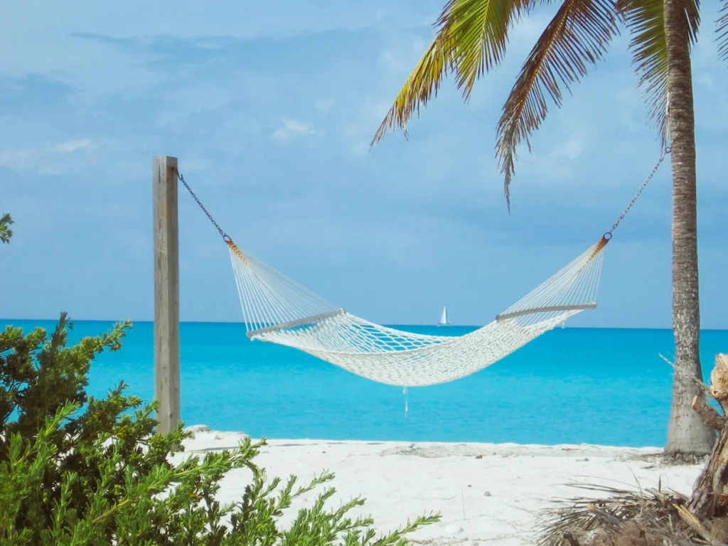 White rope hammock strung between a wooden post and a palm tree on a white sand beach in the Bahamas