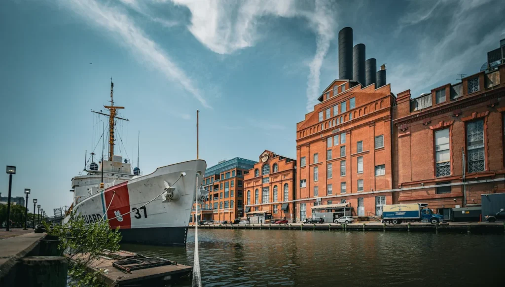 Coast Guard cutter ship docked in a canal across from historic brick industrial buildings under a blue sky