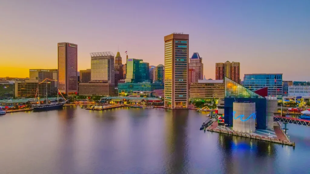 Downtown Baltimore skyscrapers rising behind the National Aquarium and Inner Harbor water at sunset