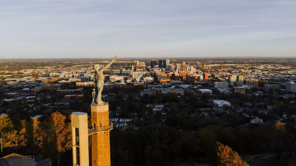 Vulcan statue standing on a tall brick pedestal overlooking the Birmingham Alabama skyline at sunset