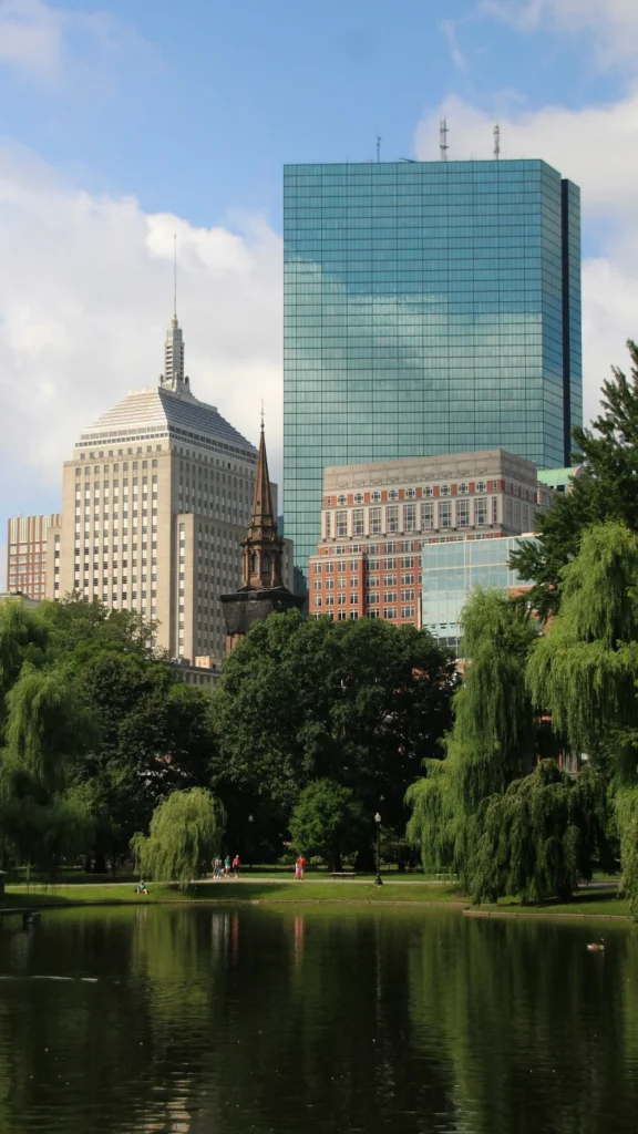 John Hancock Tower and historic city buildings rising behind the trees and pond of Boston Public Garden