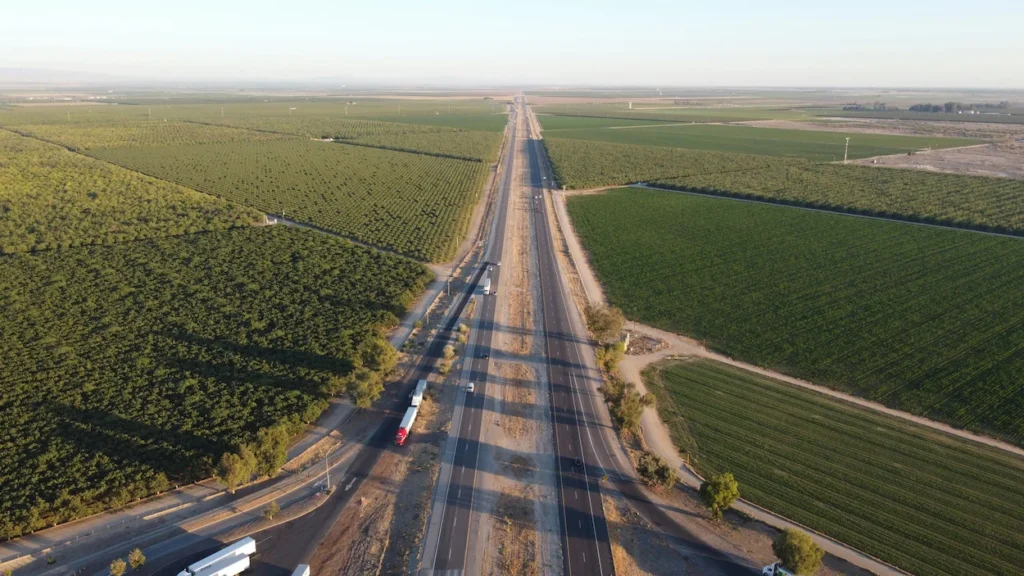 Aerial view of a multi-lane highway cutting straight through vast, green agricultural fields under a clear sky