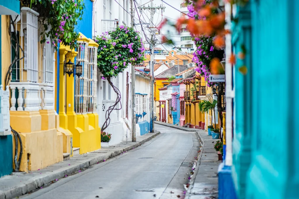 Vibrant colorful buildings and blooming bougainvillea lining a narrow paved street in Cartagena